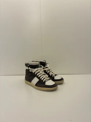 Svarta och vita high top sneakers från Saint Laurent - Snygga high top sneakers i svart och vitt med vita snören och kontrasterande detaljer. Ovandelen är i mocka och läder, och sulan är beige. Perfekta för dig som vill ha en stilren och sportig look. Förutom att dom är riktigt schyssta är det ett litet skav på hälen.                                                             (Skorna är ikonen Lars-Olas gamla!).                     Kom DM vid intresse🙌🏽