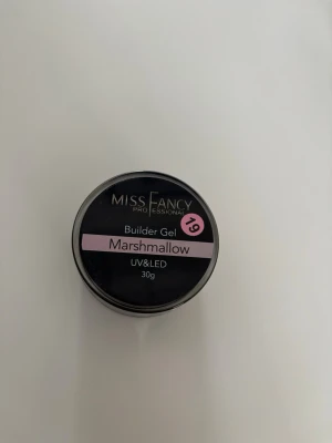 Miss Fancy Builder Gel Marshmallow - Bygggel för naglar från Miss Fancy i nyansen Marshmallow. Gelén är i hög viskositet! Därför ser det ut som att jag har använt den mycket men det har jag inte utan dig jämnar bara inte ut sig i burken. Gelen är ljusrosa och passar för UV och LED-härdning. Perfekt för att skapa snygga och hållbara naglar. Förpackningen innehåller 30g gel i en rund burk.