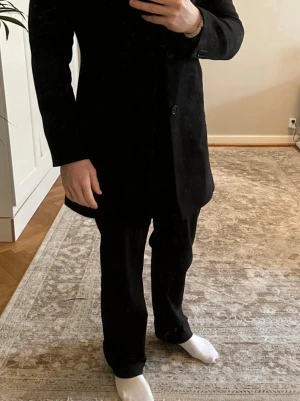 Svart klassisk rock från Filippa K - Stilren svart rock från J.Lindeberg med enkelknäppning och klassisk krage. Rocken har en rak passform och är tillverkad i ett slätt tyg som ger en elegant look. Perfekt för dig som gillar minimalistisk och tidlös stil. Storlek 48/Medium