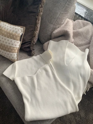 Vit ribbad omlottklänning - Säljer en vit ribbad omlottklänning med korta ärmar och hjärtformad-ringning. Klänningen har en snygg struktur i tyget och är i en mjuk, stretchig kvalitet som formar sig efter kroppen. Perfekt för dig som gillar minimalistisk och stilren design. Har en tråddragning på insidan (syns inte på utsidan) därför valt bra skick, övrigt som ny. 