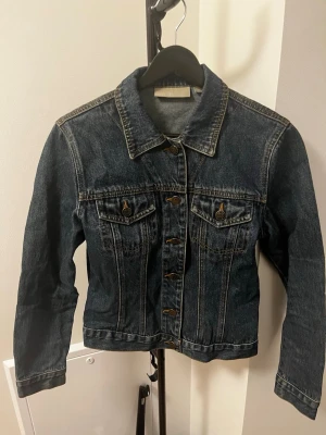 Mörkblå klassisk jeansjacka - Snygg mörkblå jeansjacka med klassisk passform och kontrastsömmar. Två bröstfickor med knappar framtill och knappstängning hela vägen. Perfekt att slänga över en hoodie eller t-shirt för en avslappnad look.