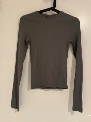 Grå ribbad långärmad topp BikBok - En stilren grå långärmad topp från BikBok i ribbat material. Modellen är figurnära med rund halsringning och passar perfekt till jeans eller kjol. Enkel och snygg bas till garderoben.
