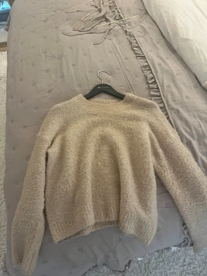 Beige fluffig stickad tröja - Mysig beige stickad tröja med fluffig textur och rund hals. Tröjan har långa ärmar och ribbade muddar vid ärmslut och nederkant. Perfekt för kalla dagar när du vill vara både varm och snygg. Liten i storleken, sitter som en s på mig som brukar ha s 