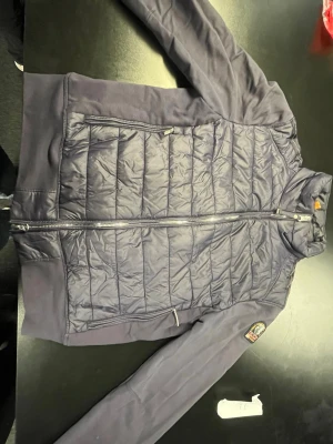 Mörkblå dunjacka från Parajumpers - Snygg mörkblå dunjacka från Parajumpers med quiltat mönster på framsidan och släta ärmar. Jackan har dragkedja framtill, två sidofickor med dragkedja och en patch med logga på ärmen. Perfekt för kalla vinterdagar.