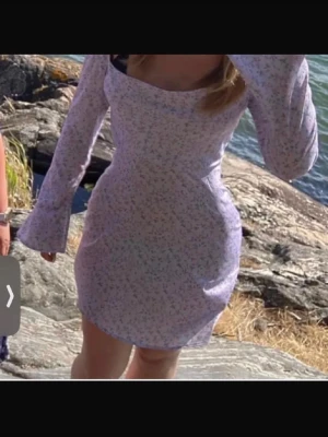 Ljuslila blommig kort klänning - Superfin ljuslila kort klänning med småblommigt mönster och långa ärmar. Klänningen har en figurnära passform och en snygg, något fyrkantig urringning. Perfekt för vår och sommar!