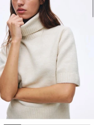 Beige stickad polotröja med kort ärm - Snygg beige stickad polotröja med korta ärmar och bred ribbad mudd i midjan och vid ärmslut. Tröjan har en hög polokrage. Endast använd 1 gång på grund av att jag ej tycker polo tröjor passar mig. Slutsålda i alla storlekar upp till M (se bild 4) inga tecken på användning, ser ut som ny. Krämvit färg.