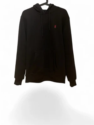 Svart hoodie från Ralph Lauren - Svart hoodie från Ralph Lauren med klassisk huva och dragsnören. Liten röd broderad logga på bröstet och stor känguruficka framtill. Mjuk bomullsblandning och ribbade muddar vid ärmslut och nederkant. Perfekt för en avslappnad och stilren look.