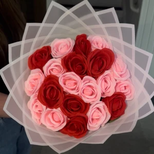 Blombukett - En vacker bukett med konstgjorda rosor i rött och rosa, omsorgsfullt arrangerade och inslagna i transparent papper med dekorativ kant. Perfekt som present eller dekoration till hemmet.