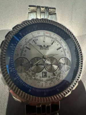 Softech silverfärgad kronografklocka - Stilren kronografklocka från Softech i silverfärg med blå ring runt urtavlan. Klockan har flera små urtavlor, datumvisning och metallänk. Perfekt accessoar för dig som gillar detaljer och en sportig men elegant look. Funkar ej! 