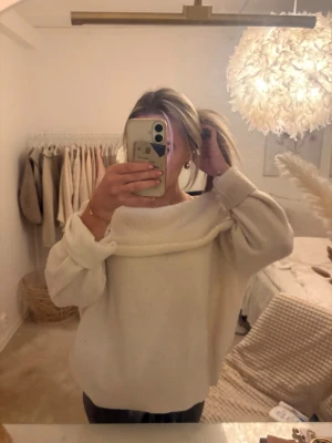 Off shoulder vit stickad tröja - Trendig vit stickad tröja med off shoulder-design och bred krage. Tröjan har en avslappnad passform och långa ärmar, perfekt för en mysig och stilren look.