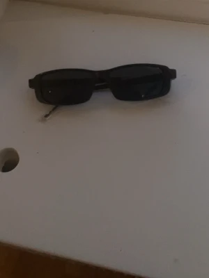 Svarta rektangulära solglasögon - Säljer ett par svarta solglasögon med rektangulära glas och smala metallbågar. Snygg minimalistisk design som passar till många olika stilar. Perfekta för soliga dagar!