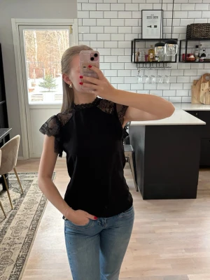 Svart blus med spetsdetaljer - Snygg svart blus med spetsärmar och spets vid halsringningen. Blusen har korta ärmar med volang och en liten knappöppning i nacken. Publicerad på flera säljsidor 🌸