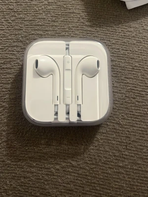 Vita Apple EarPods med sladd - Säljer ett par klassiska vita Apple EarPods med sladd och inbyggd fjärrkontroll för volym och samtal. Snygg och stilren design i plast, levereras i originalförpackning. Perfekta för musik, poddar och samtal på språng.
