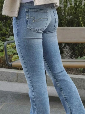 Ljusblå bootcut jeans från Junkyard - Säljer ett par ljusblå jeans från Junkyard i bootcut. Jeansen har klassiska bakfickor med dekorativ söm, normalhög midja och bälteshällor. Tillverkade i slitstark denim med snygg tvättad look. Perfekta för en avslappnad och trendig stil.