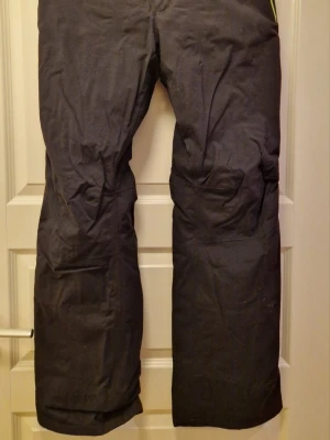 Svarta täckbyxor Peak Performance M - Svarta skidbyxor från Peak Performance. Byxorna har raka ben, förstärkta knän och dubbla knappar i midjan. Perfekta för vinterns alla äventyr och håller dig både varm och torr.