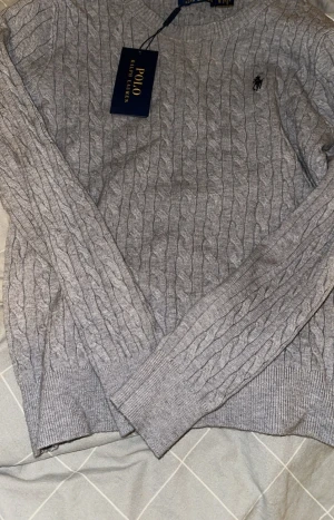 Grå kabelstickad tröja Polo Ralph Lauren - Passar om du är runt 160-165 och runt 45-55kg Kabelstickad grå tröja från Polo Ralph Lauren.