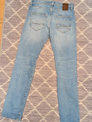Jack & Jones jeans - Säljer ett par ljusblå jeans från Jack & Jones i storlek 29/32. Modellen är Slim/Glenn. Sista bilderna är defekter, ena är vid den vänstra bakfickan andra vid grenen. Det stör inte användningen och har ej blivit hål. Kontakta gärna vid frågor!😊