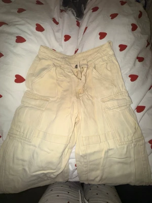 Beige cargobyxor med fickor - Säljer ett par beige cargobyxor med stora sidofickor. Byxorna är högmidjade o har avslappnad passform och är tillverkade i ett mjukt bomullsliknande material. Perfekta för en chill och casual stil. Uppsydda för att passa 135-145💛