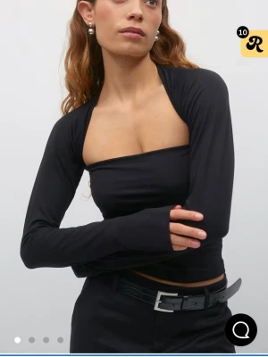 Svart soft touch  square topp med lång ärm - Helt ny med prislapp. Cool svart bolerotopp med långärmad design och öppen rygg. Toppen är croppad och har en unik form som framhäver axlarna. Perfekt för dig som vill sticka ut med en trendig och edgy look. Storlek S. Nypris 279kr. 