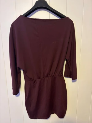 Vinröd kort klänning med trekvartsärm - En enkel och stilren vinröd kort klänning med trekvartsärm och markerad midja. Klänningen har en lös passform upptill och är tillverkad i ett mjukt material som känns bekvämt mot huden. Perfekt för dig som gillar minimalistisk stil. Pris kan diskuteras. Använt en gång!