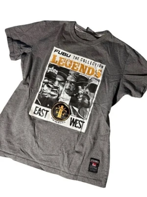 Grå FUBU Legends t-shirt med tryck - Snygg grå t-shirt från FUBU med stort grafiskt tryck på framsidan med texten 'Legends' och motiv av kända hiphop-profiler. Klassisk passform, rund hals och korta ärmar. Materialet är mjuk bomull och märkeslapp finns nertill. even it says small the it can fit medium