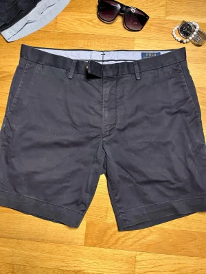 Mörkblå shorts från Polo Ralph Lauren - Snygga svarta shorts från Polo Ralph Lauren med stretch och slim fit-passform. Klassisk design med bälteshällor och diskreta fickor, perfekta för en stilren look under varma dagar.