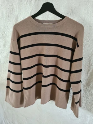 Beige tröja med svarta ränder - Snygg beige tröja med svarta horisontella ränder och rund hals. Tröjan har en avslappnad passform och långa ärmar. Perfekt för en stilren och enkel look. Materialet känns mjukt och bekvämt mot huden.