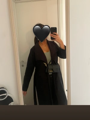 Svart lång vårkappa med skärp - Snygg svart lång vårkappa med brett slag och knytband i midjan. Kappan har en avslappnad passform och är perfekt för lager på lager. Passar till alla tillfällen och ger en clean look. Nypris 500kr och nu säljer jag för 170kr