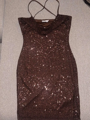 Brun paljettklänning från NA-KD - Snygg brun klänning från NA-KD med tunna axelband och täckt av glittriga paljetter. Modellen är figurnära och croppad, materialet känns dock mjukt och stretchigt😍 