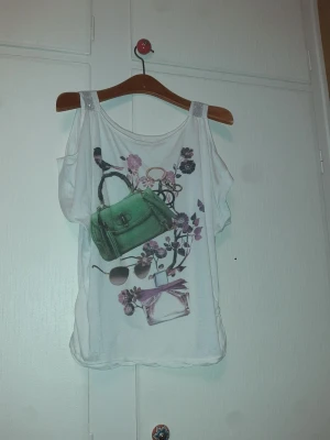 Vit linnetopp med print - Vit linnetopp med färgglatt print av grön väska, solglasögon, parfymflaska och blommor i lila och rosa. Toppen har breda axelband och ärmlös design, perfekt för en trendig och avslappnad look.