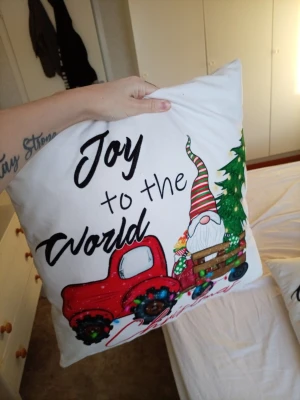 Julig kuddfodral med tomte och röd bil -  kuddefodral med vit botten, motiv av röd bil, tomte i randig luva och gran. Texten 'Joy to the World Christmas' tryckt på framsidan. Perfekt som julpynt i soffan eller sängen. Färgglad design i bomullsliknande material. Dom ä 45X45cm priset ä för båda 