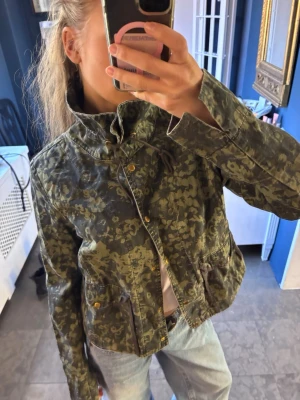 Grön blommig vårjacka - Grön blommig vårjacka med knappar fram till samt krage som kan knytas eller has nere.