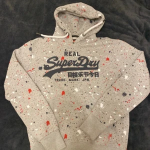 Superdry hoodie - Säljer en grå hoodie från Superdry med skit schyst paint splatter. Den är storlek M och sitter bra. Ställ gärna frågor.
