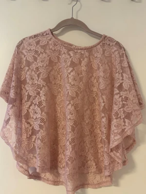 Rosa spetsblus med vid passform - Säljer en ljusrosa blus i spets med blommigt mönster. Blusen har vid och lös passform, rund halsringning och är kortärmad. 