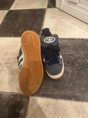 Mörkblåa addidas campus ! - Snygga blå sneakers från Adidas med vita ränder på sidorna och stort Adidas-logotyp på plösen. Skorna har breda mörkblå skosnören och en klassisk gummisula i brunt. Ovandelen är i mockaliknande material och designen är sportig och retro. Pris går absolut att diskutera 💕