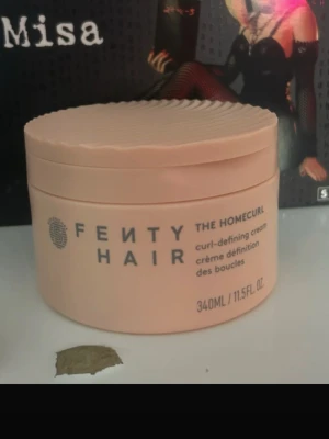 Fenty Hair The Homecurl kräm - Fenty Hair The Homecurl curl-defining cream i en ljusbeige rund burk på 340 ml. Produkten är en kräm för att definiera och återfukta lockar, perfekt för dig som vill ha mjuka och återfuktade lockar som står emot fukt. Snygg vågig design på locket.