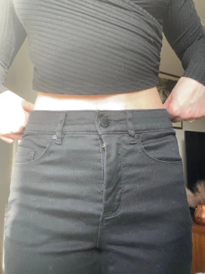 Svarta jeans med hög midja - Snygga svarta  jeans med hög midja och klassisk femficksdesign. Jeansen har bälteshällor och stängs med knapp och dragkedja. Perfekta till en trendig vardagslook och passar till det mesta i garderoben.