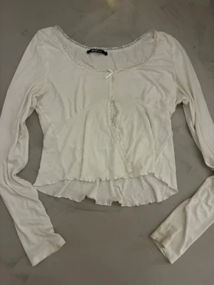 Vit långärmad croppad topp med spets - Säljer en vit långärmad croppad topp från Gina tricot med spetsdetaljer runt halsen och längs mitten.