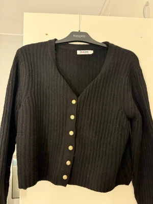 Svart ribbad kofta - Stilren svart ribbad kofta från J'aime, köpt på Missäy i Göteborg med långa ärmar och guldknappar framtill. Perfekt att matcha med jeans eller kjol. Pris kan diskuteras. Aldrig använt. Tror ny pris va 400. Storleken är S/M men skulle säga att den är S. 