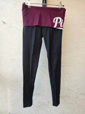 Svarta tights från Victoria's Secret Pink - Svarta yogatights/leggings från Victoria's Secret Pink i storlek XS. Vinröd kant som man viker över så går att justera hur höga de är i midjan. Kanppt använda, i fint skick.