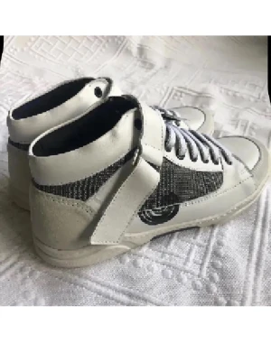 Vita höga skinn  sneakers med meshdetaljer - Snygga vita sneakers med högt skaft, svarta meshdetaljer på sidorna och kardborreband över vristen. Skorna har vita snören och en svart logga på sidan. Materialmix av läder, mocka och mesh ger en modern look.