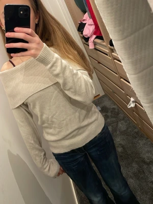 Beige off shoulder tröja - Säljer en beige off shoulder tröja med bred ribbad krage som går över axlarna. Tröjan har långa ärmar och ribbade muddar vid ärmslut och nederkant. Perfekt för dig som gillar en stilren och trendig look.
