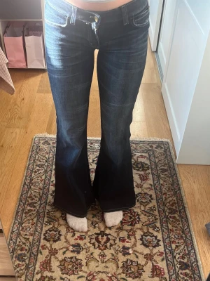Mörkblå bootcut jeans - Säljer ett par mörkblå bootcut jeans med låg midja och klassiska fem fickor. Jeansen har en snygg tvätt och utsvängda ben som ger en retrovibe. Perfekta för dig som gillar en avslappnad men trendig stil.