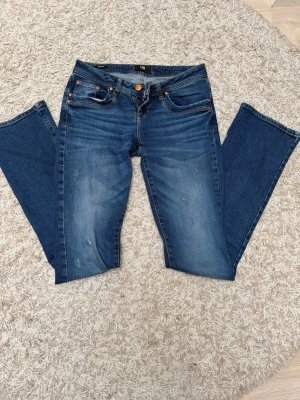 Blå bootcut jeans från LTB - Snygga blå bootcut jeans från LTB med klassisk femficksmodell och slitningar framtill. Jeansen har en mellanblå tvätt med ljusare partier och kontrastsömmar. 