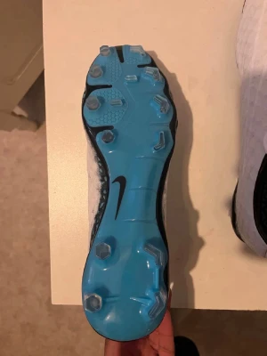 Nike fotbollsskor med blå sula - Snygga fotbollsskor från Nike med en iögonfallande ljusblå sula och svarta detaljer. Skorna har fasta dobbar för bra grepp på planen och en modern, sportig design. Perfekta för dig som vill sticka ut på fotbollsplanen.