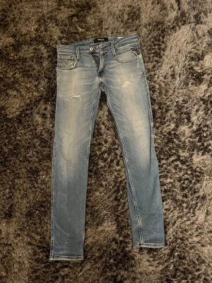 Replay Anbass 29/32 - Säljer ett par ljusblå jeans från Replay med slitningar på låren och knäna. Slitningarna har kommit med tiden av användning men brallorna är ju fortfarande as feta. Materialet är mjukt denim med stretch för extra komfort. Förutom dom slitningarna där för är det även ett litet litet hål där bak precis där vänster ficka är. Är det några frågetecken är de bara att skriva? ✍️ 