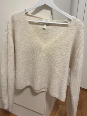Krämvit stickad tröja från H&M - Mysig krämvit stickad tröja från H&M med djup v-ringning och långa ärmar. Tröjan har en mjuk, ribbstickad struktur och avslappnad passform som gör den enkel att styla till olika outfits. Passar till de flesta från mjukisbyxor till jeans eller kjol. Skriv gärna ifall ni skulle vilja ha fler bilder. Pris går att diskutera.