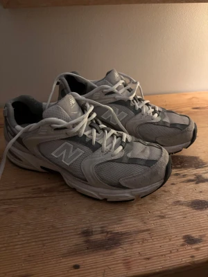 Grå New Balance sneakers - Säljer ett par klassiska grå New Balance sneakers med vita detaljer och meshpaneler för extra ventilation. Skorna har den ikoniska N-loggan på sidan och en chunky sula som ger skön komfort. Perfekta för dig som gillar retrostil och streetwear. Jätte sköna dojor passar till allt. Nypris 1550