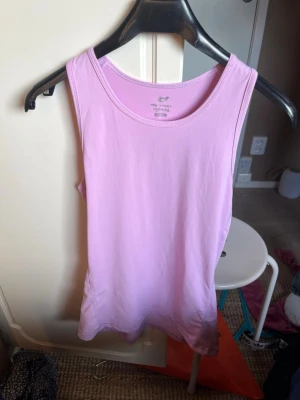 Ljuslila träningstopp från H&M - Säljer en enkel och stilren ljuslila linnetopp från H&M. Toppen är ärmlös med rund halsringning och har en mjuk, stretchig känsla. Perfekt att matcha med jeans eller kjol för en avslappnad look.