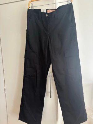 NYA! Svarta cargobyxor  - OANVÄND! Säljer ett par svarta cargobyxor  med raka ben och flera praktiska fickor på sidorna. .